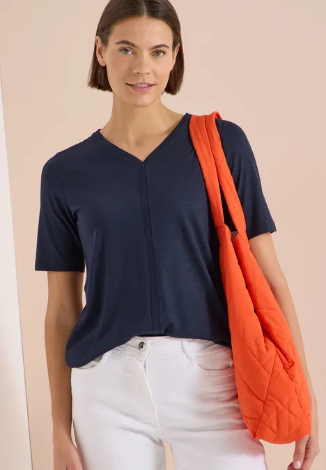 Kurzarm T-Shirt im Tunika-Look universal blue Eine Frau trägt ein dunkelblaues V-Shirt, weiße Hose und eine orange Stepp-Shopper-Tasche.