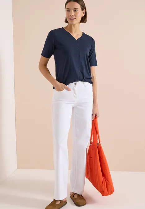 Kurzarm T-Shirt im Tunika-Look universal blue Frau trägt marineblaues V-Shirt, weiße Hose, braune Schuhe und hält orangefarbene Tasche.