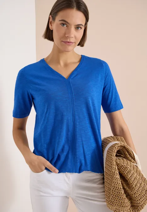 Kurzarm T-Shirt im Tunika-Look surf blue Frau in blauem V-Ausschnitt-T-Shirt und weißen Hosen hält einen geflochtenen Korb.