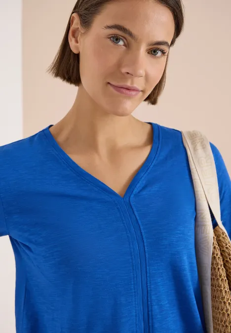 Kurzarm T-Shirt im Tunika-Look surf blue Eine Person trägt ein leuchtend blaues Oberteil mit V-Ausschnitt und eine Strohtasche über der Schulter.