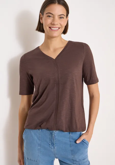 Kurzarm T-Shirt im Tunika-Look brown cacao Eine Person trägt ein braunes V-Ausschnitt-Shirt mit kurzen Ärmeln und steckt die Hand in die Jeans.