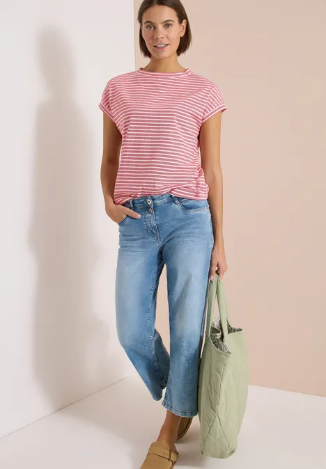 Eine Frau trägt eine rote gestreifte Bluse, weite blaue Jeans und hält eine grüne Tasche.