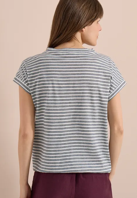 Achteraanzicht van iemand met een grijs-wit gestreept T-shirt en bordeauxrode broek tegen lichte achtergrond.