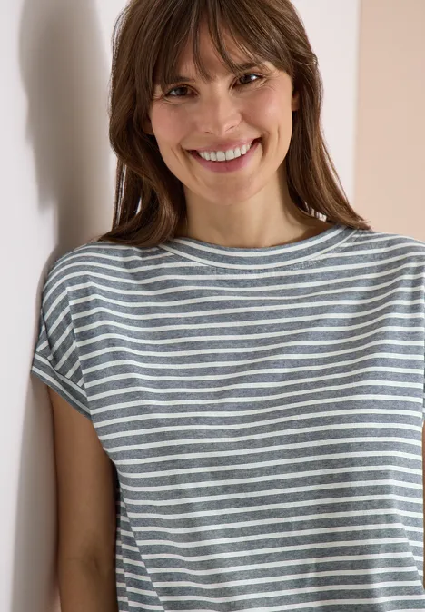 Iemand staat tegen een muur en draagt een grijs-wit gestreept T-shirt.