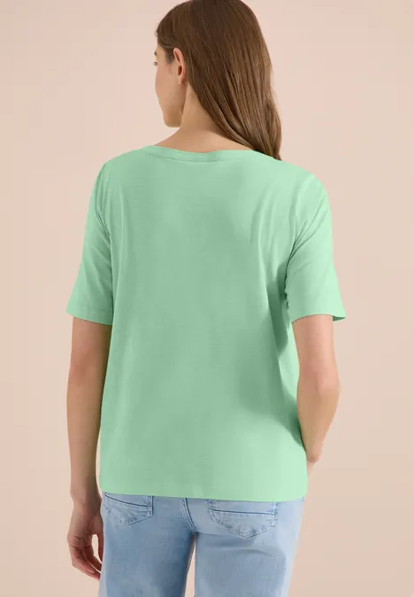 Frau steht mit dem Rücken zur Kamera, trägt ein hellgrünes T-Shirt und blaue Jeans.