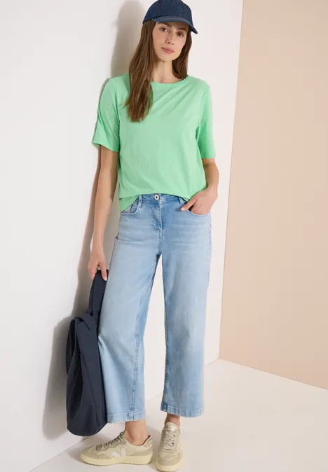 Frau trägt mintgrünes T-Shirt, weite blaue Jeans, Sneaker und lässige Tasche.