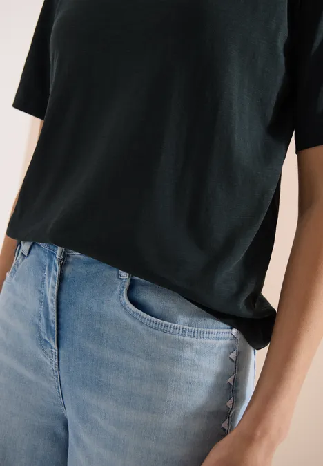 Person trägt schwarzes T-Shirt und helle Jeans, Nahaufnahme von Oberkörper und Händen.