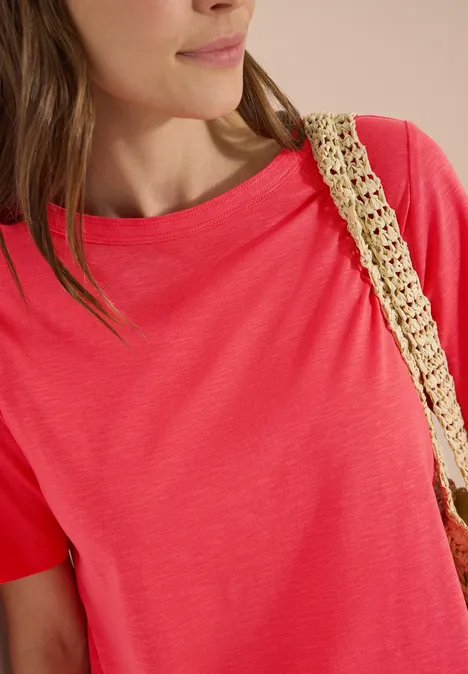 Kurzarm T-Shirt aus reiner Baumwolle coral Nahaufnahme einer Frau in korallfarbenem T-Shirt mit gewebtem Strohtaschen-Träger.