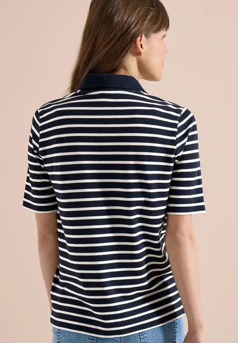 Eine Person von hinten in einem blau-weiß gestreiften kurzärmeligen Poloshirt vor beigem Hintergrund.