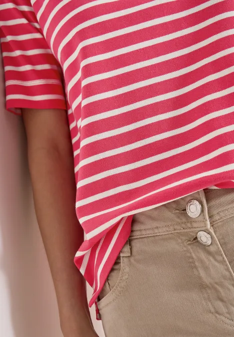 Eine Person trägt ein rosafarbenes T-Shirt mit weißen Streifen und beige Hose.