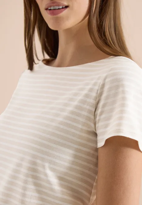 Eine Frau trägt ein beiges, gestreiftes T-Shirt vor beigem Hintergrund.