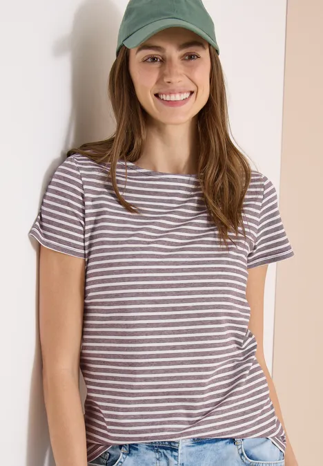 Junge Frau mit grüner Mütze und gestreiftem T-Shirt lehnt lässig an einer Wand.