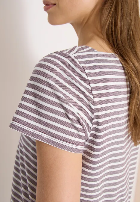 Seitliche Aufnahme einer Frau mit braunen Haaren im weiß-lila gestreiften T-Shirt vor weißem Hintergrund.