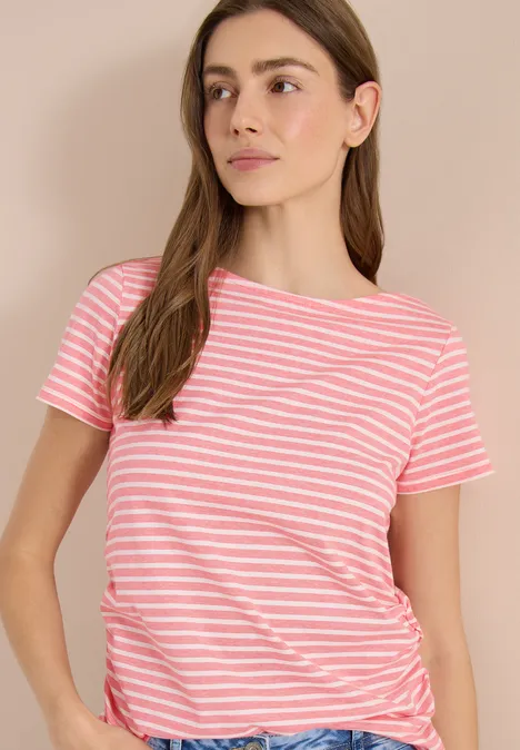 Eine junge Frau trägt ein rosa-weiß gestreiftes T-Shirt mit kurzen Ärmeln vor neutralem Hintergrund.