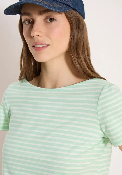 Een persoon met een turquoise-wit gestreept t-shirt en een donkerblauwe baseballpet voor een lichte achtergrond.