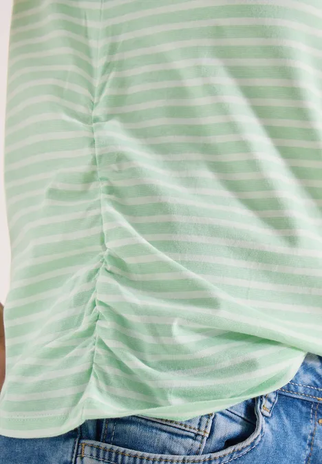 Groen-wit gestreept T-shirt met zijsamengetrokken plooien, gecombineerd met een blauwe spijkerbroek.