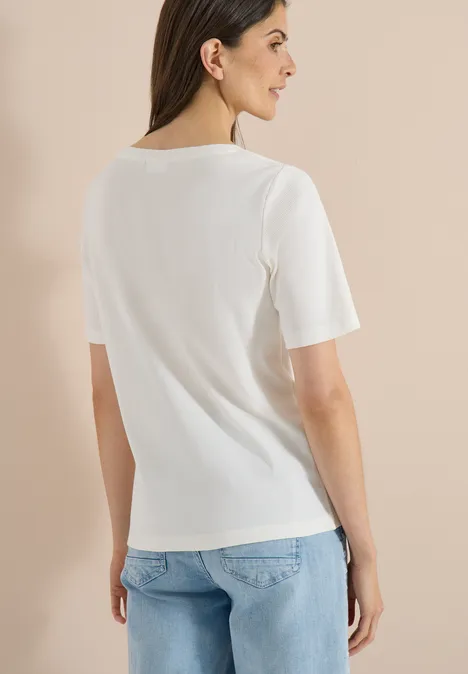 Frau von hinten in weißem T-Shirt und hellblauen Jeans vor beigem Hintergrund.