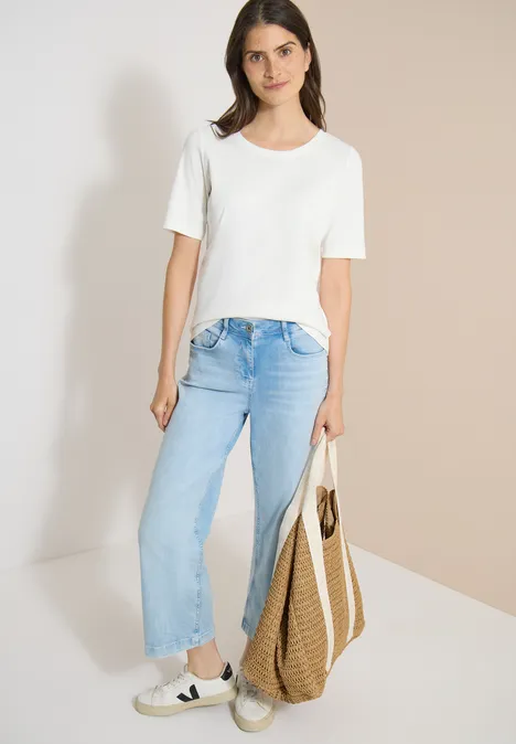 Frau im lässigen Outfit: weißes T-Shirt, hellblaue Jeans, Sneakers und Strohtasche.