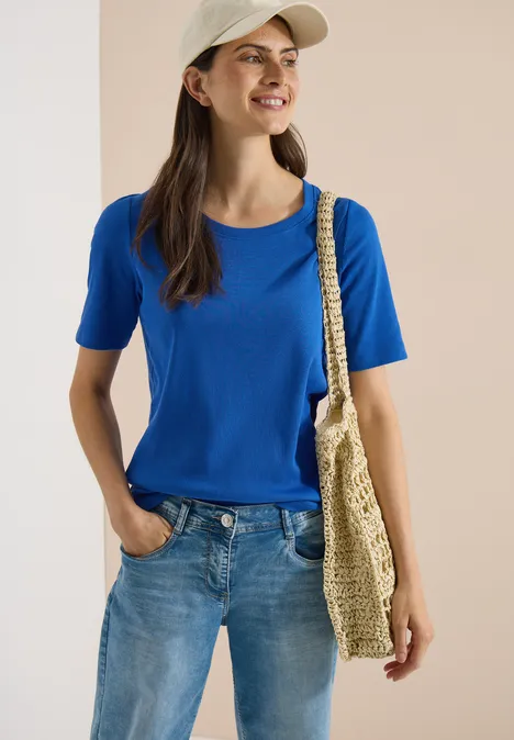 Basic Shirt met geribde textuur surf blue Vrouw in blauw T-shirt en spijkerbroek, met stro tas en pet, staat nonchalant met één hand in de zak