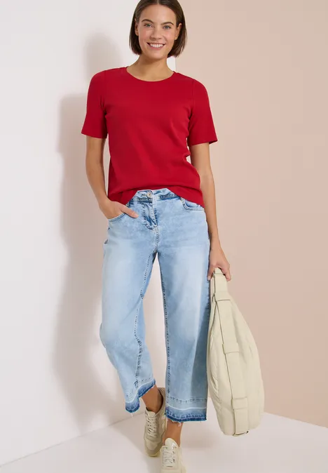 Frau in rotem T-Shirt und hellblauen Jeans hält Tasche.