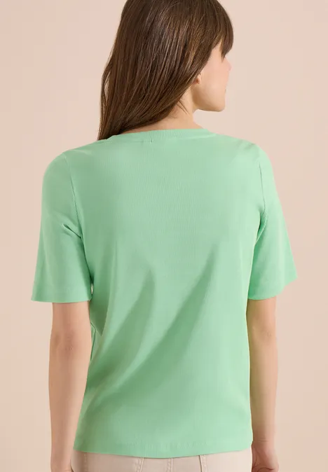 Basic geribd Shirt juicy lime Vrouw van achteren in lichtgroen shirt met korte mouwen, neutrale achtergrond.