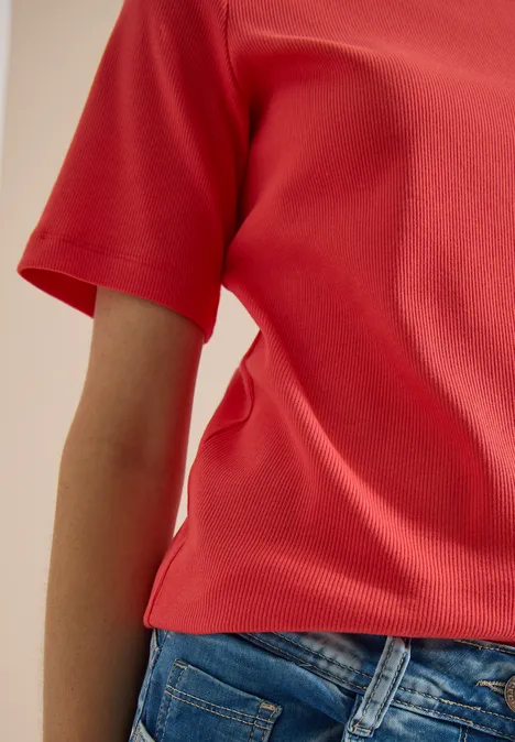 Eine Person trägt ein rotes Shirt und blaue Jeans, Teilansicht des Oberkörpers