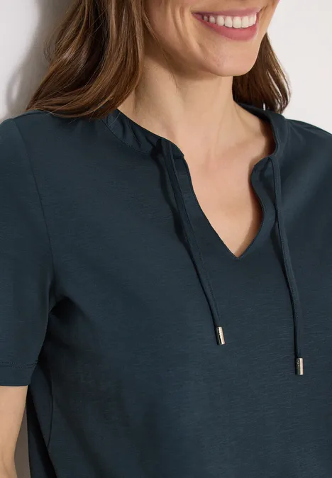 Frau in dunkelblauer Kurzarmbluse mit V-Ausschnitt und Bindeband, sie lächelt.