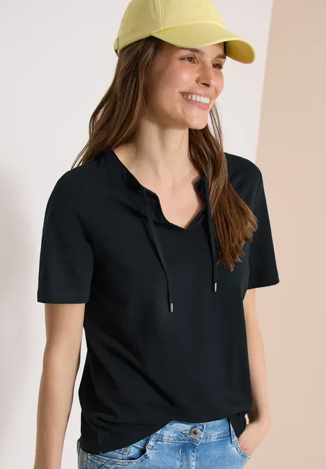 Junge Person in schwarzem Kurzarm-Shirt mit Kapuze, gelber Cap und blauen Jeans.