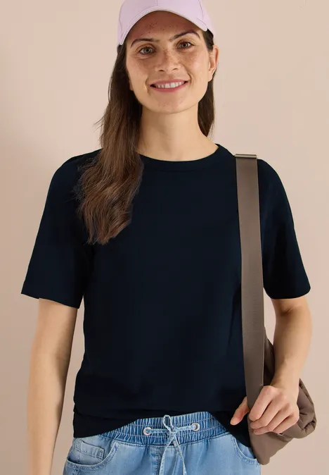 Shirt met strepen in een 2-pack vanilla white/universal blue Vrouw in donkerblauw T-shirt met korte mouwen, bruine schoudertas, effen beige achtergrond.