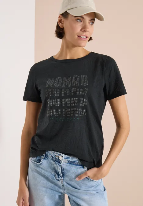 Shirt met korte mouwen in burnout-look palm breeze green Vrouw met vervaagd gezicht draagt donkergrijs T-shirt met 'NOMAD'-opdruk en blauwe jeans voor een lichte achtergrond