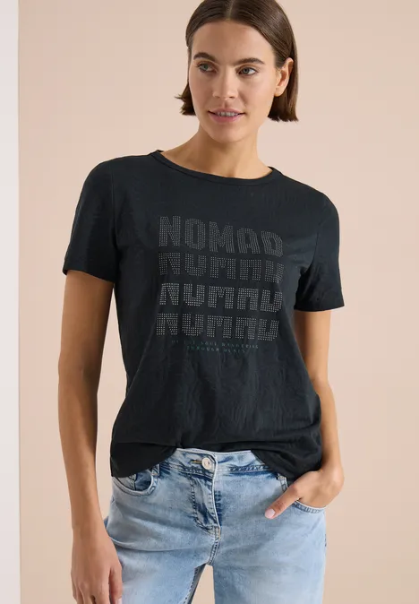 Shirt met korte mouwen in burnout-look palm breeze green Een persoon draagt een zwart t-shirt met herhaald 'NOMAD'-logo en een lichtblauwe spijkerbroek.