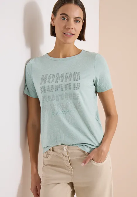 Shirt met korte mouwen in burnout-look crystal mint Een vrouw draagt een mintgroen T-shirt met 'Nomad Journal'-opdruk en een beige broek, hand in zak.