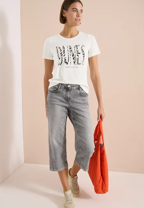 T-Shirt mit Rundhals und Frontprint vanilla white Frau im weißen Print-T-Shirt, grauen Culotte-Jeans, Sneakern und orangefarbener Tasche.