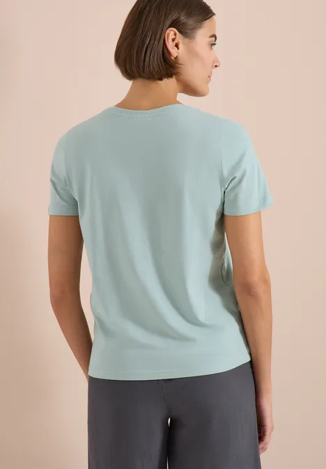 T-Shirt mit Rundhals und Frontprint crystal mint Frau von hinten in hellblauem T-Shirt und dunkler Hose vor neutralem Hintergrund.