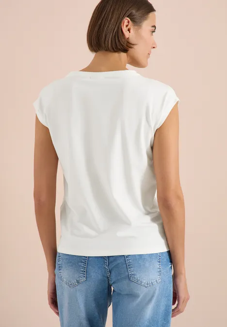 Rückansicht einer Frau in weißem T-Shirt und blauen Jeans vor einfarbigem Hintergrund.