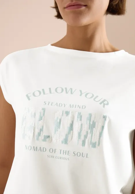 Frau trägt weißes T-Shirt mit pastellfarbenem Schriftzug und Grafik auf der Vorderseite.