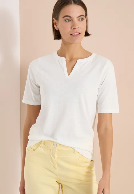 Shirt met gespleten hals in effen kleur vanilla white Een vrouw draagt een wit V-hals T-shirt en lichtgele jeans tegen een neutrale achtergrond.