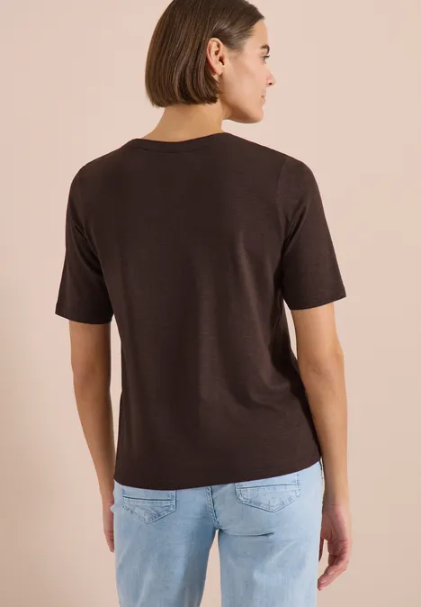 T-Shirt mit Split Neck in Unifarbe brown cacao Frau von hinten in braunem T-Shirt mit Halbarm und hellblauer Jeans vor beigem Hintergrund.