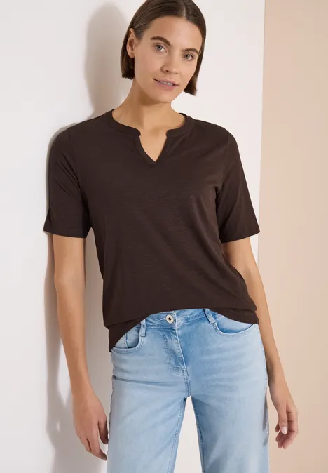 T-Shirt mit Split Neck in Unifarbe brown cacao Eine Person in dunklem T-Shirt mit V-Ausschnitt und hellen Jeans vor hellem Hintergrund.