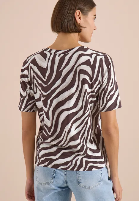 T-Shirt mit Split Neck mit Print brown cacao Person von hinten in schwarz-weißem Zebramuster-T-Shirt und hellblauer Jeans vor beigem Hintergrund.