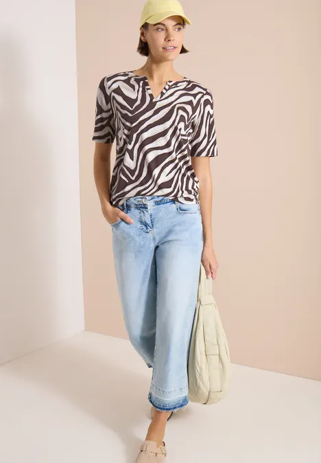 T-Shirt mit Split Neck mit Print brown cacao Person trägt zebra-gestreiftes T-Shirt, helle Jeans, hält beige Tasche.