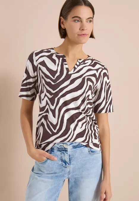 T-Shirt mit Split Neck mit Print brown cacao Frau trägt schwarz-weiß gestreifte Zebra-Bluse mit V-Ausschnitt und kurzen Ärmeln, dazu helle Jeans.