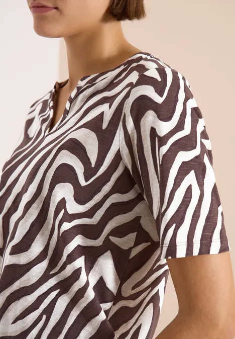 T-Shirt mit Split Neck mit Print brown cacao Eine Frau trägt ein kurzärmeliges Oberteil mit braun-weißen Zebra-Streifen.