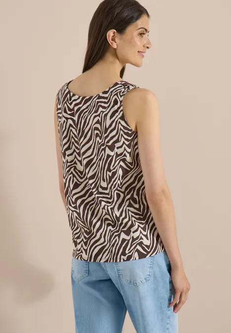 Top met ronde hals en plooidetail brown cacao Vrouw van achteren in mouwloos zebrapatroon top en lichtblauwe jeans.