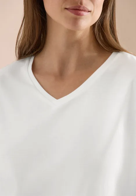 Frau trägt schlichtes weißes V-Ausschnitt-Shirt, nur Oberkörper sichtbar.