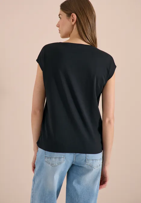 Chemise dropped shoulder avec col en V palm breeze green Frau von hinten in schwarzem Shirt und hellblauen Jeans vor neutralem Hintergrund.