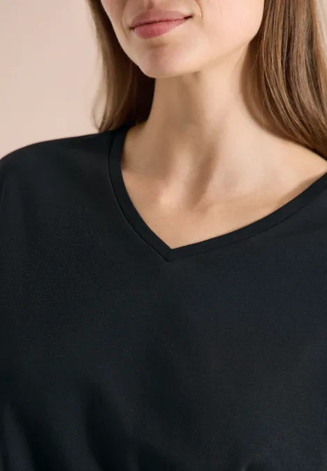 Chemise dropped shoulder avec col en V palm breeze green Eine Frau mit langen Haaren trägt ein schlichtes schwarzes V-Ausschnitt-Oberteil.