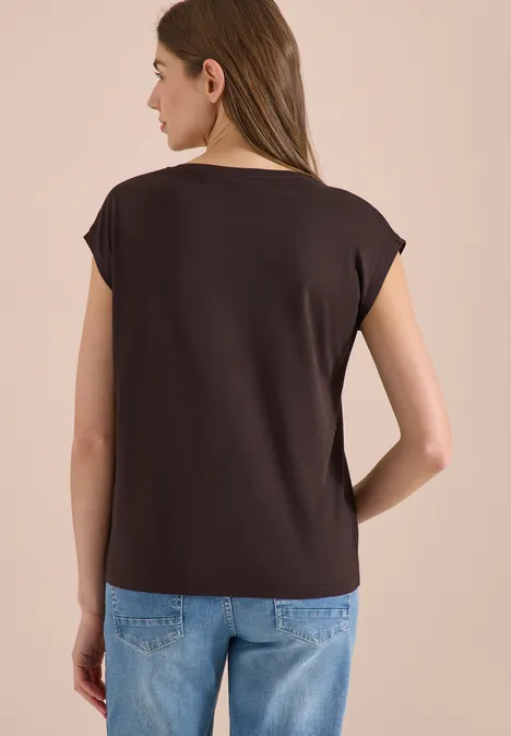 Frau von hinten in braunem T-Shirt und blauen Jeans vor hellem Hintergrund