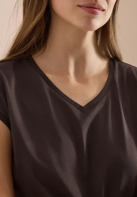 Frau mit dunkelbraunem V-Ausschnittshirt, nur Oberkörper und Teil des Gesichts sichtbar.