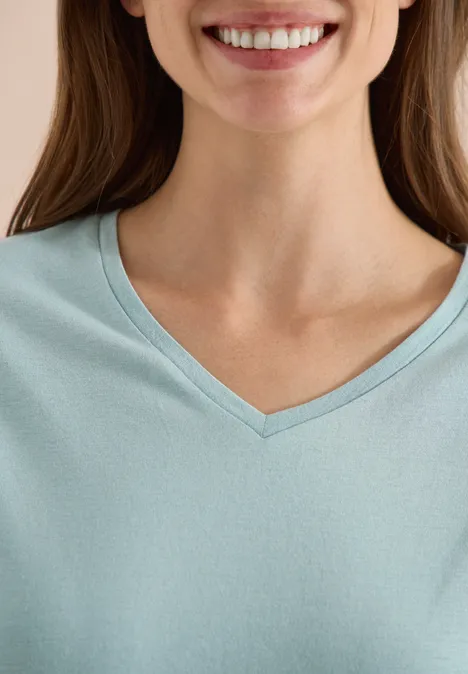 Shirt met overhangende schouders en V-hals crystal mint Glimlachende vrouw in lichtblauw V-hals T-shirt, alleen hals en borst zichtbaar.